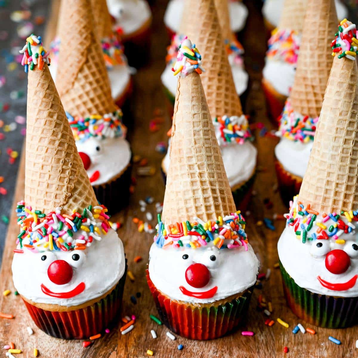 clown cupcakes with sugar ice cream cone hats on a wood platter with sprinkles