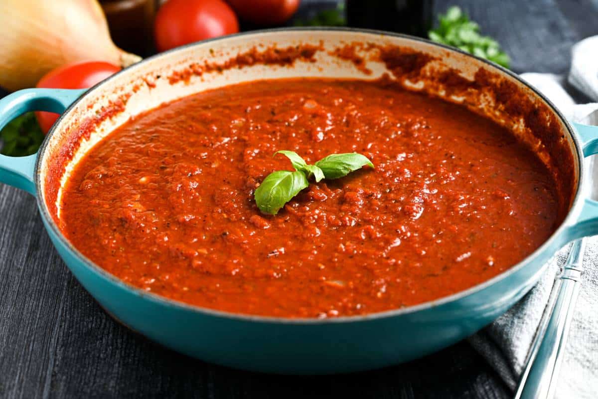 a pan of hearty marinara with vegetables and herbs in the background