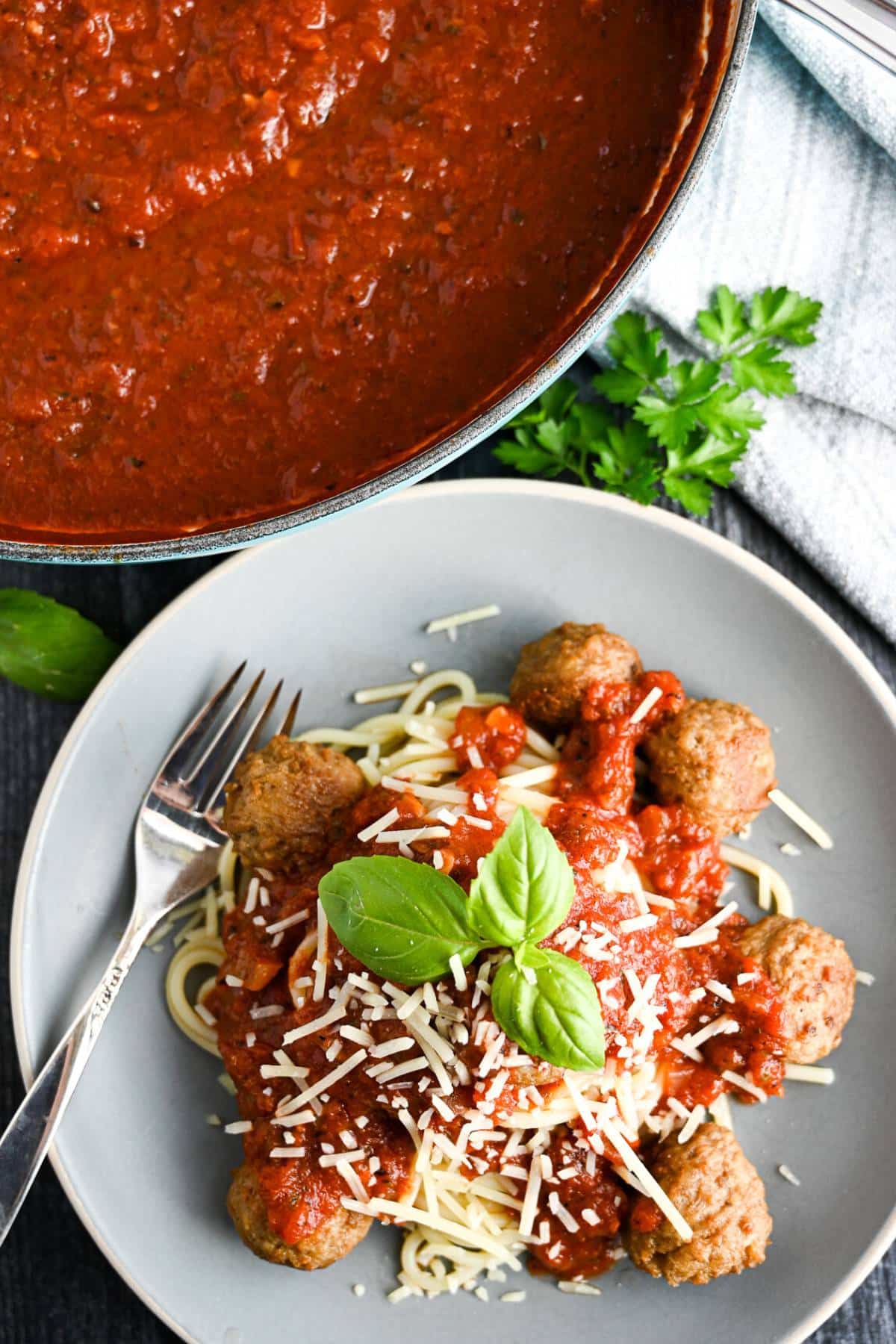 a pan of hearty marinara with a plate of spaghetti and meatballs with a sprig of basil