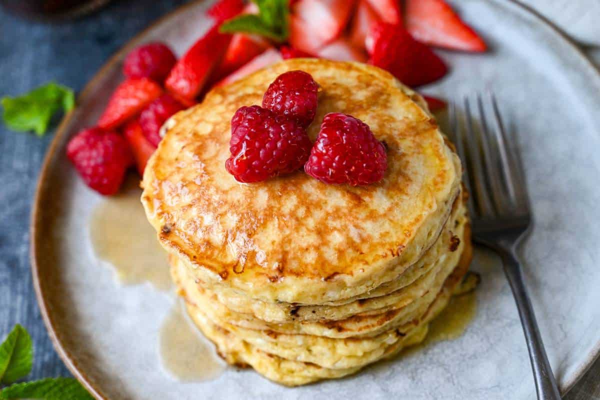 a plate of cottage cheese pancakes with a fork and berries
