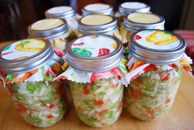 Mason jars filled with cucumber relish with decorative fabric under the lids