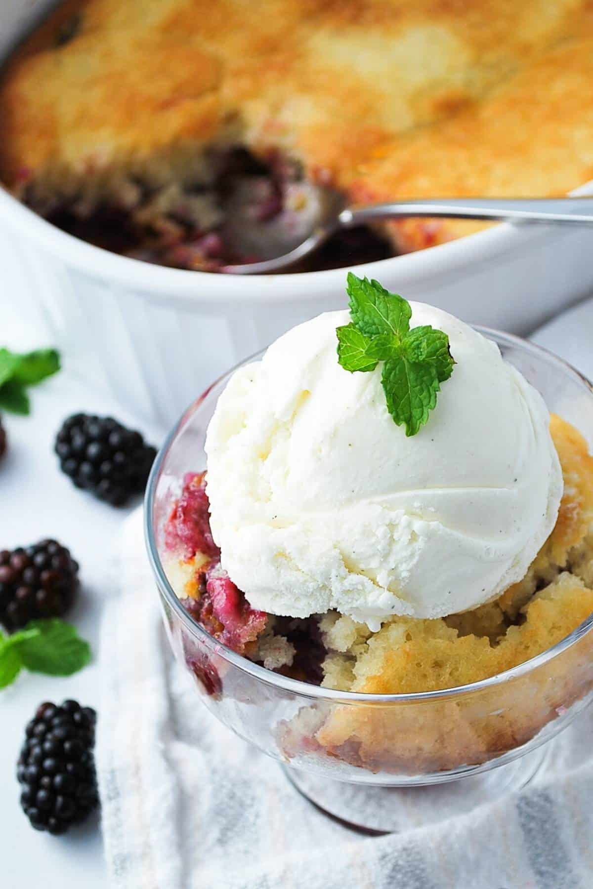 a dish of blackberry cobbler with a scoop of ice cream and fresh mint with a dish of cobbler behind it