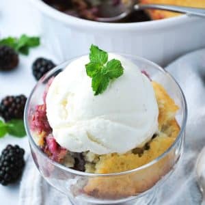 close up photo of a dish of blackberry cobbler with ice cream and a fresh mint sprig