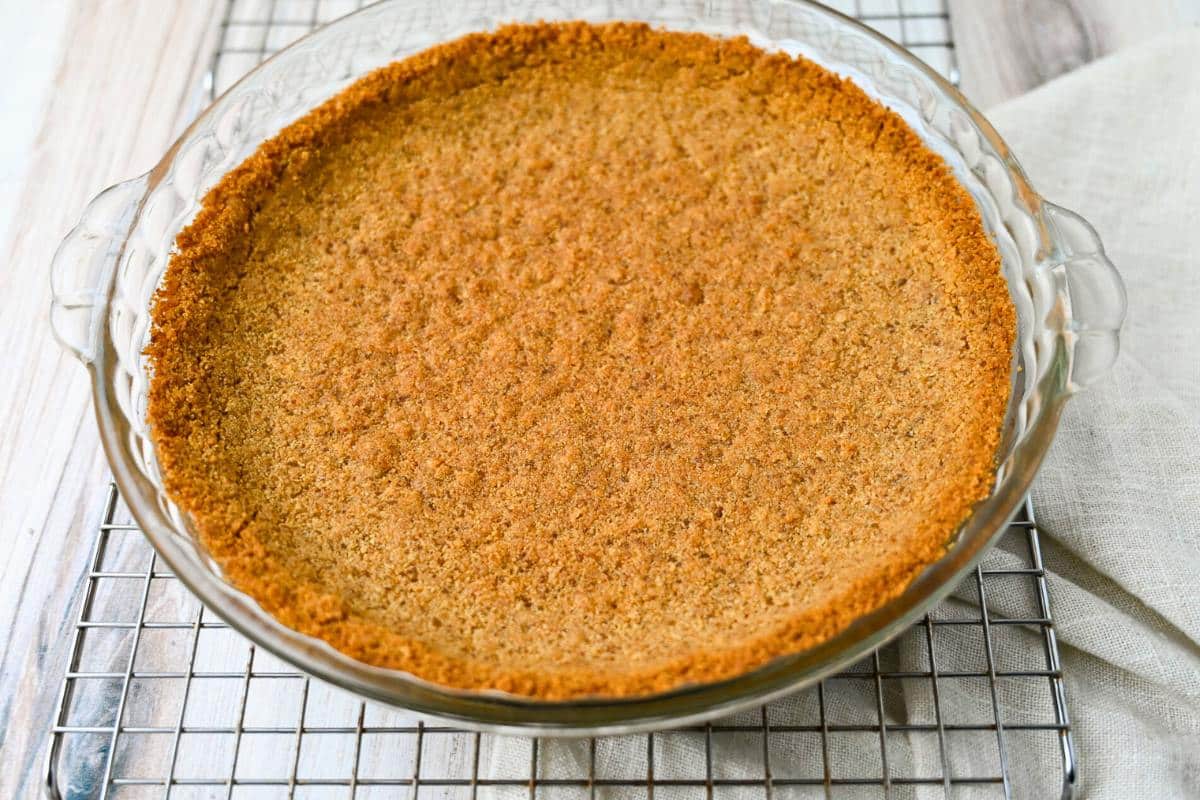 a baked graham cracker crust on a cooling rack with a towel