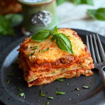 close up of a large slice of pesto lasagna on a plate with fresh basil and a fork