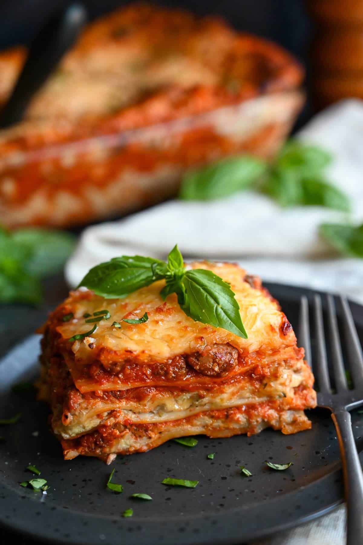 lasagna served on a plate with fresh basil garnish with the pan of lasagna in the background