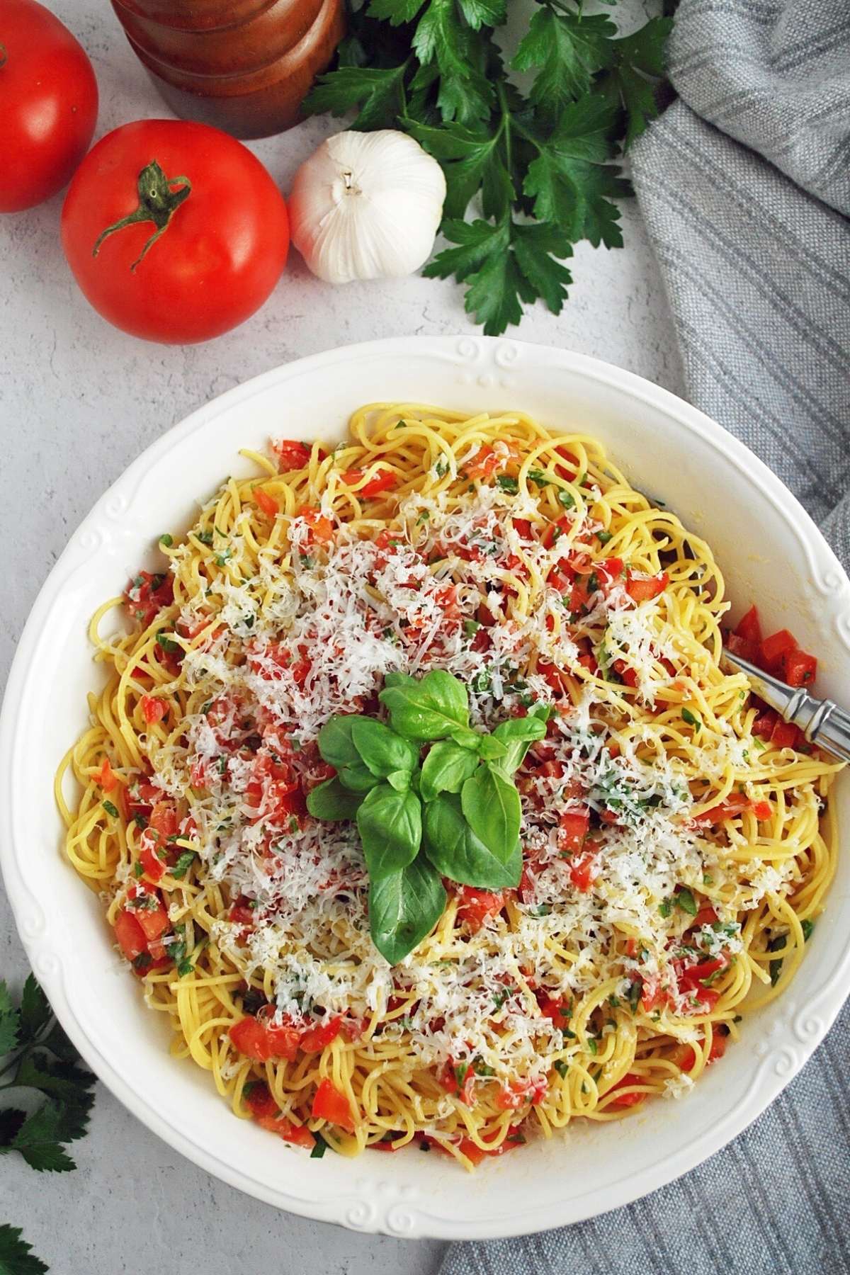 overhead photo of pasta tossed with tomato basil sauce and cheese with tomatoes, garlic, and herbs in the background