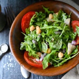 overhead photo of an arugula chickpea salad with artichoke hearts and red onion