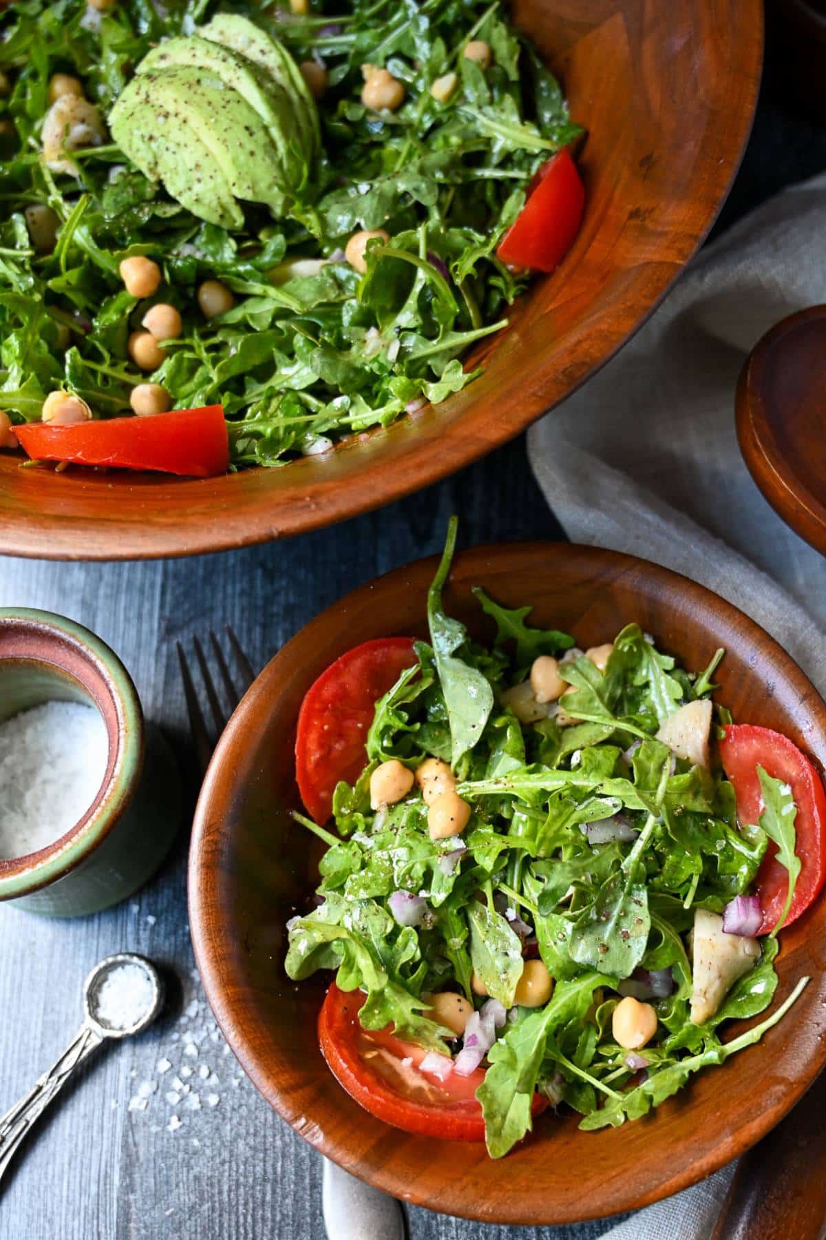 overhead photo of a small bowl of arugula salad with a serving bowl of salad with avocado on top