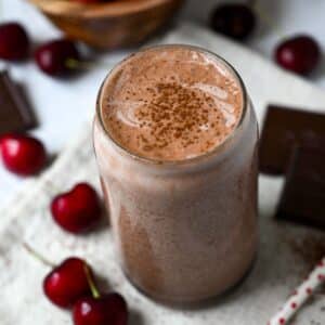 close up of a dark chocolate cherry protein shake with bing cherries around the glass and a straw