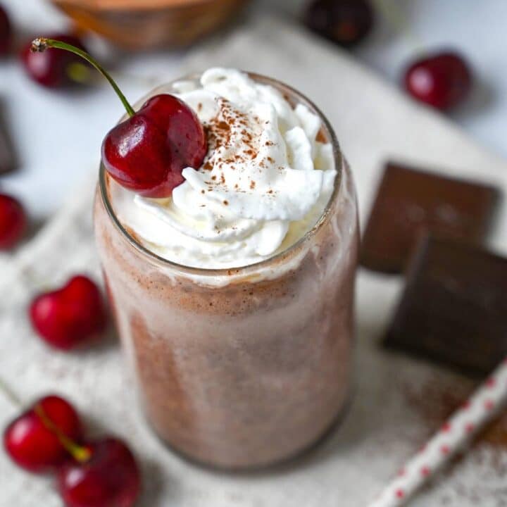 a cherry chocolate shake in a glass with whipped cream and a cherry