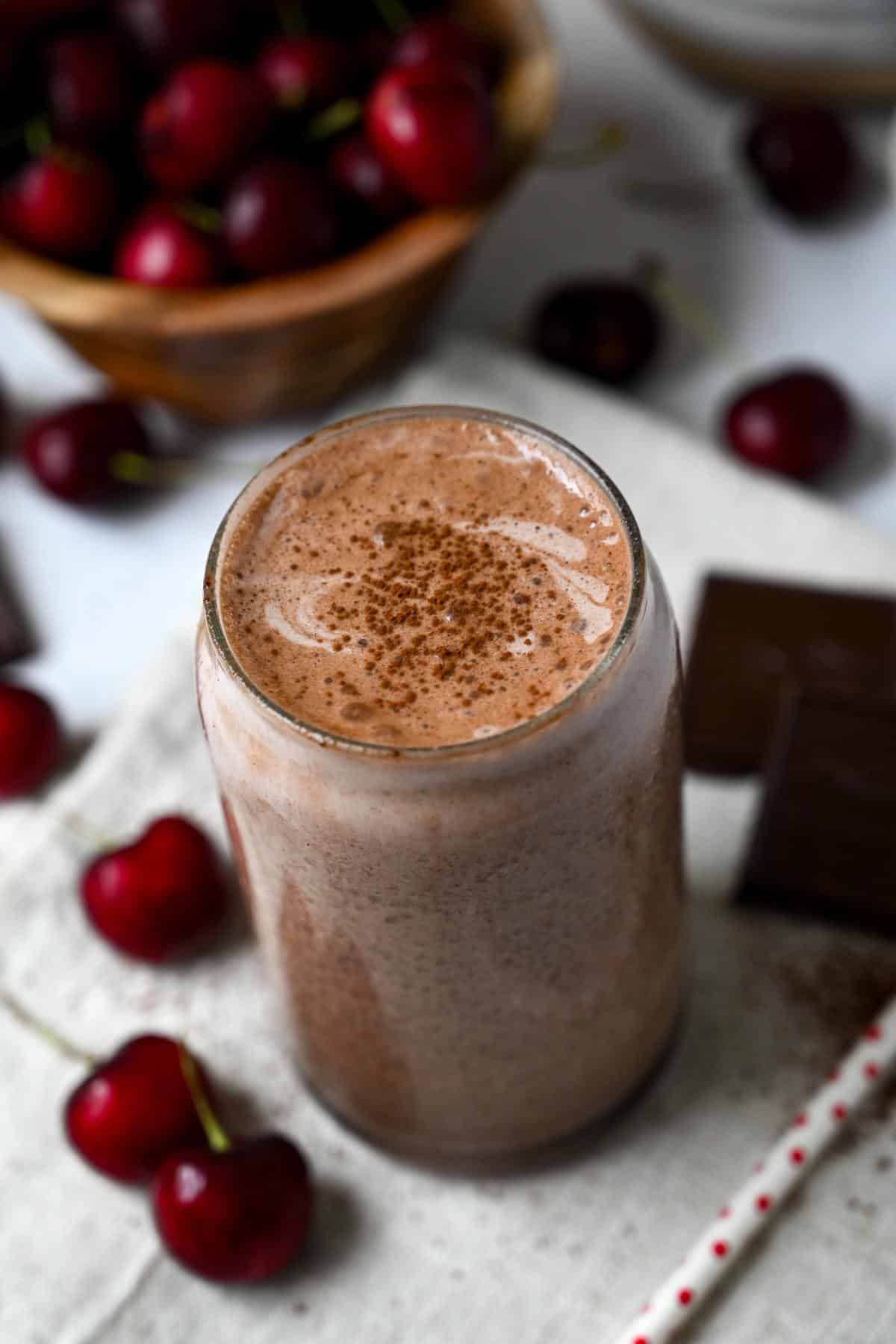 a chocolate cherry protein shake in a glass with cherries all around it