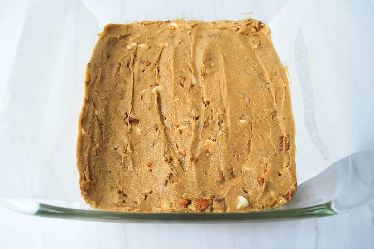 gluten free blondie batter spread in a baking dish lined with parchment paper