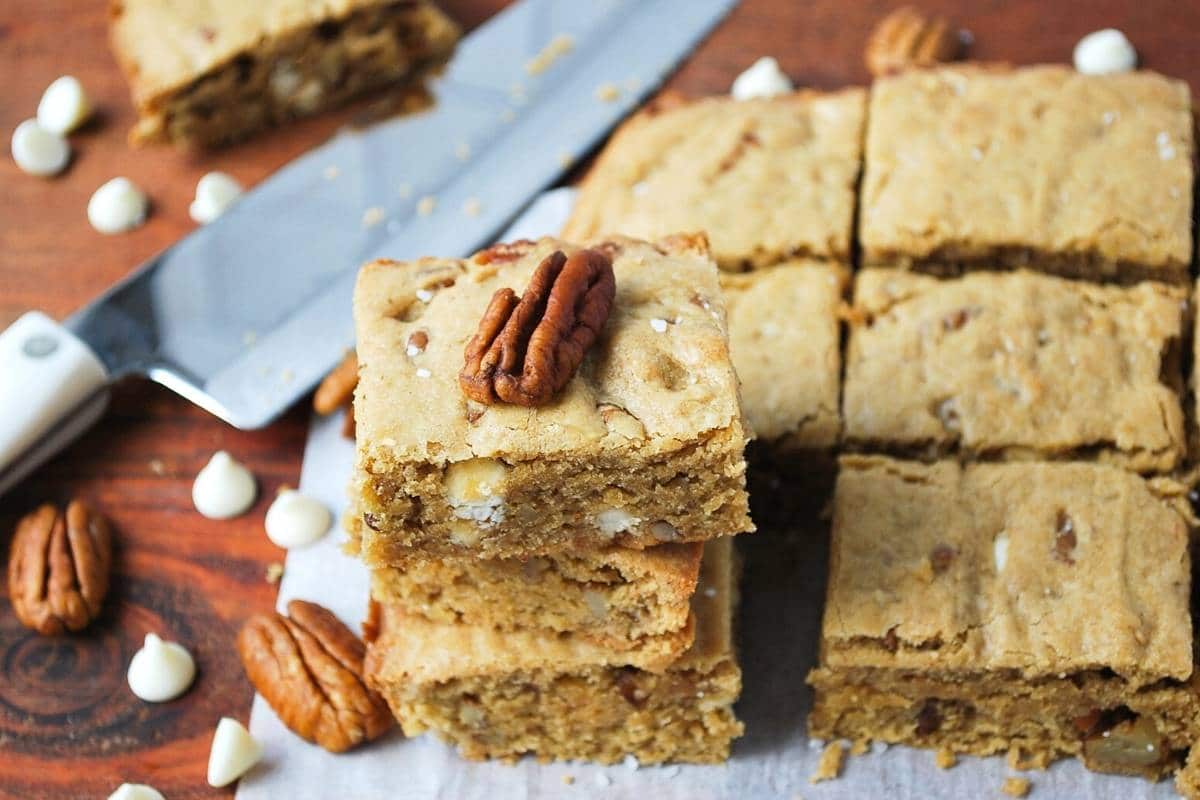 sliced gluten free blondies on parchment paper with white chocolate chips and pecans sprinkled around them