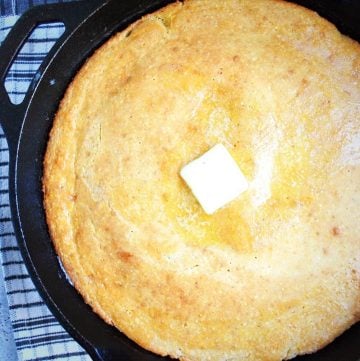 cornbread baked in a cast iron skillet with a pat of butter on top