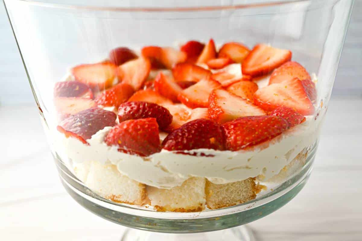 a layer of angel food cake, cheesecake filling and strawberries in a trifle bowl