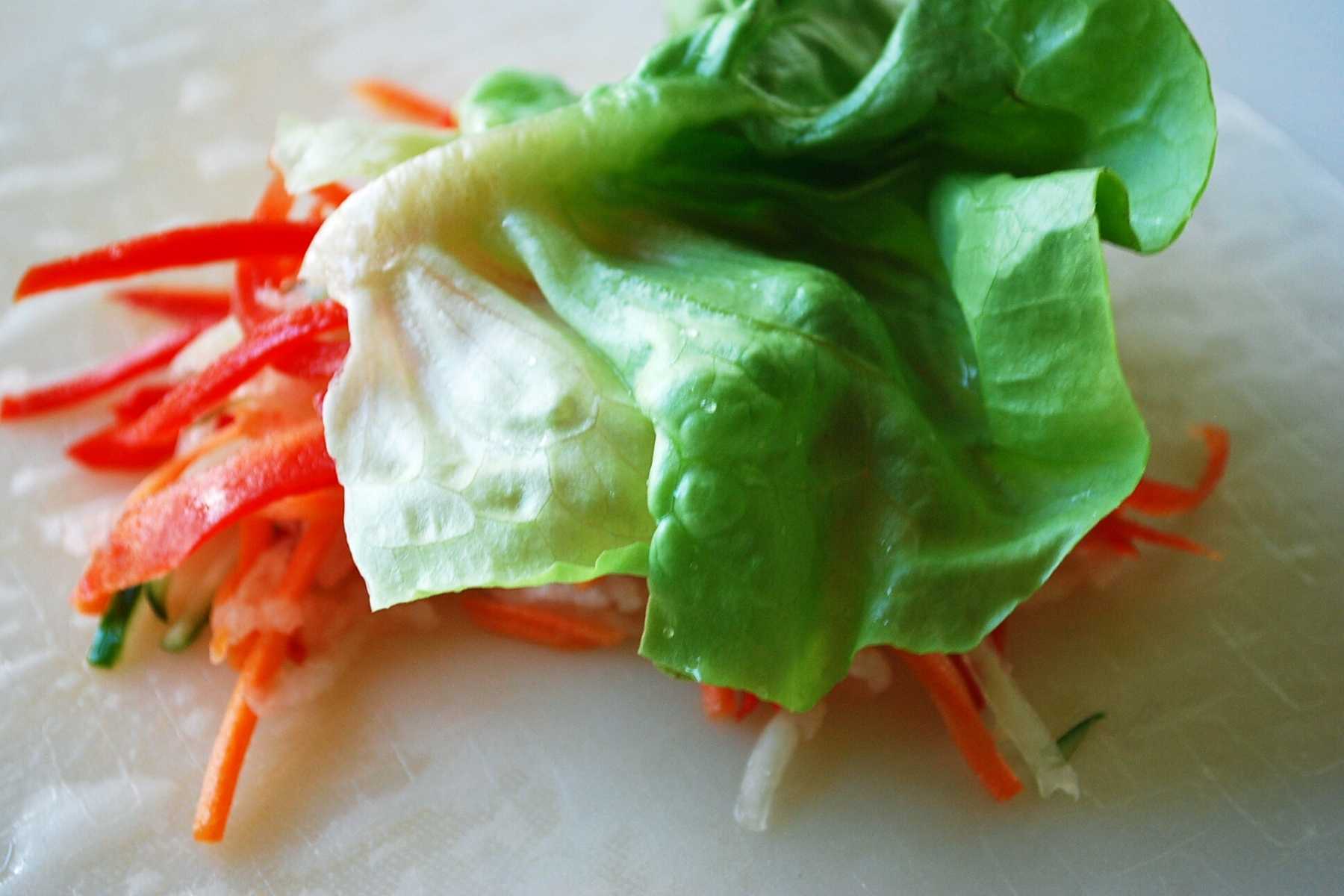 lettuce leaf on top of sliced vegetables on a rice paper wrap