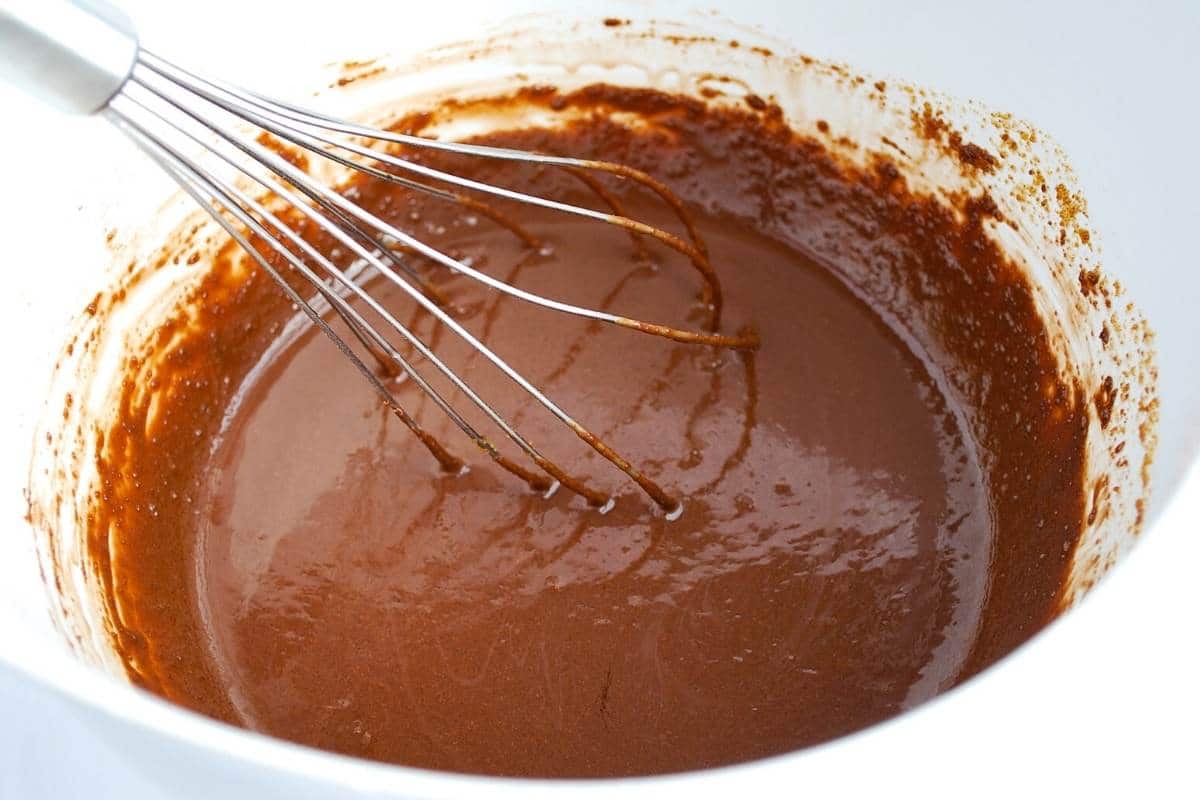 wet ingredients for protein brownies with m&ms in a white bowl with a whisk