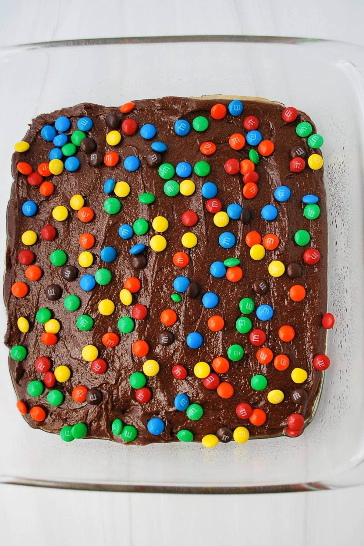 brownie batter in a glass dish topped with mini M&Ms ready to bake