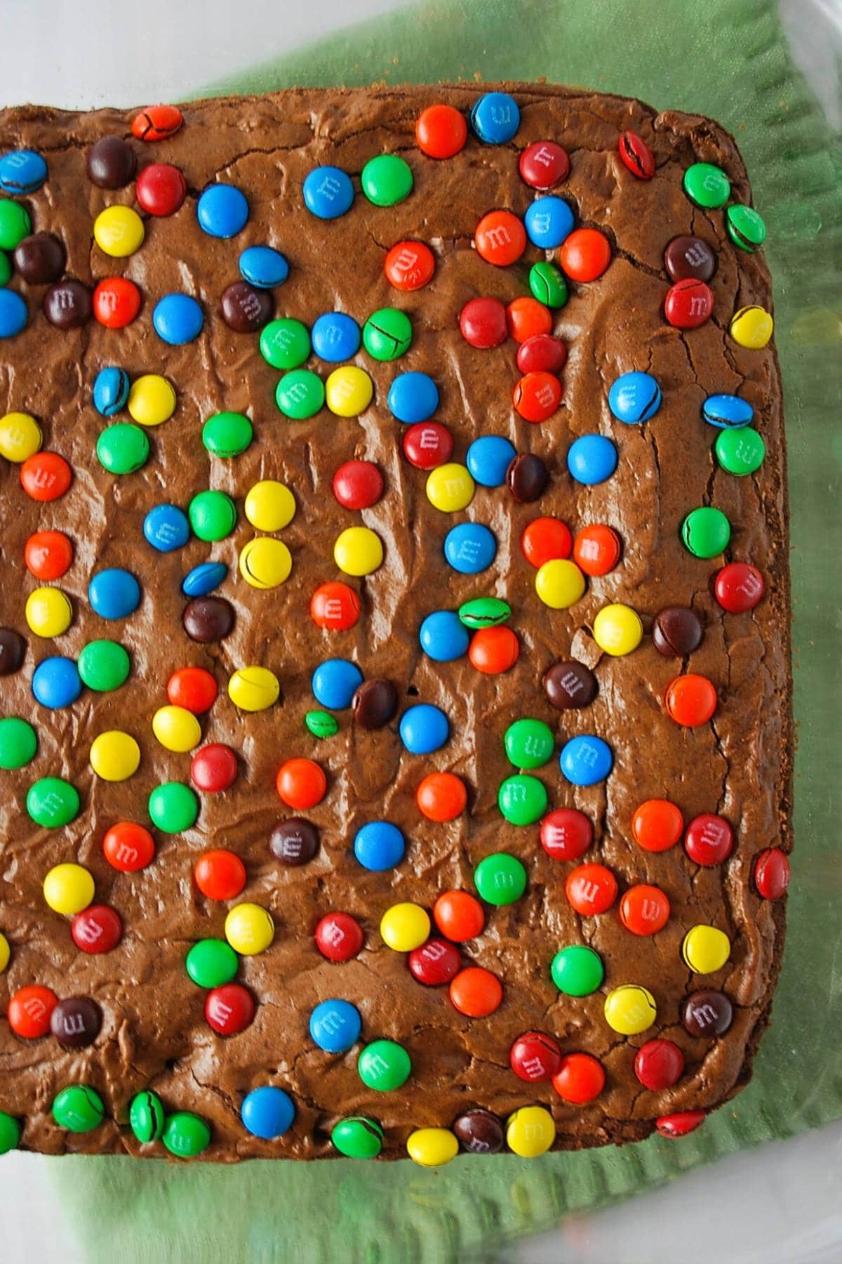 brownies topped with mini m&ms freshly baked in a glass dish with a green napkin