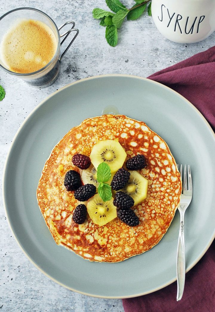 overhead shot of plated pancake with toppings, coffee and maple syrup jar