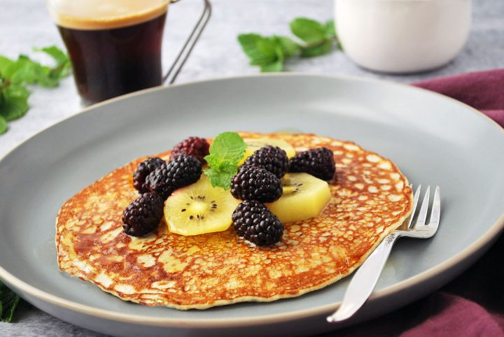 side shot of banana pancake on a plate with fork and fruit