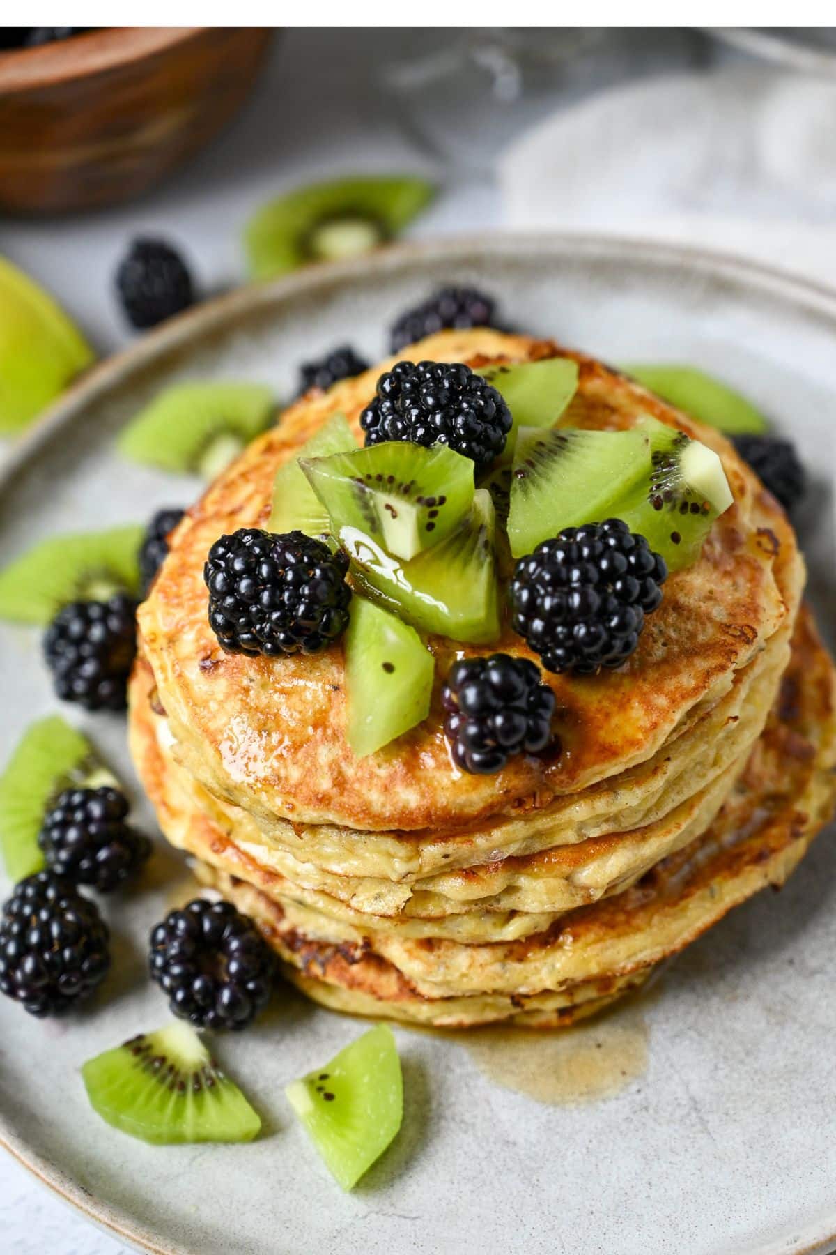 fresh kiwi fruit and blackberries on top of a stack of pancakes and around the stack