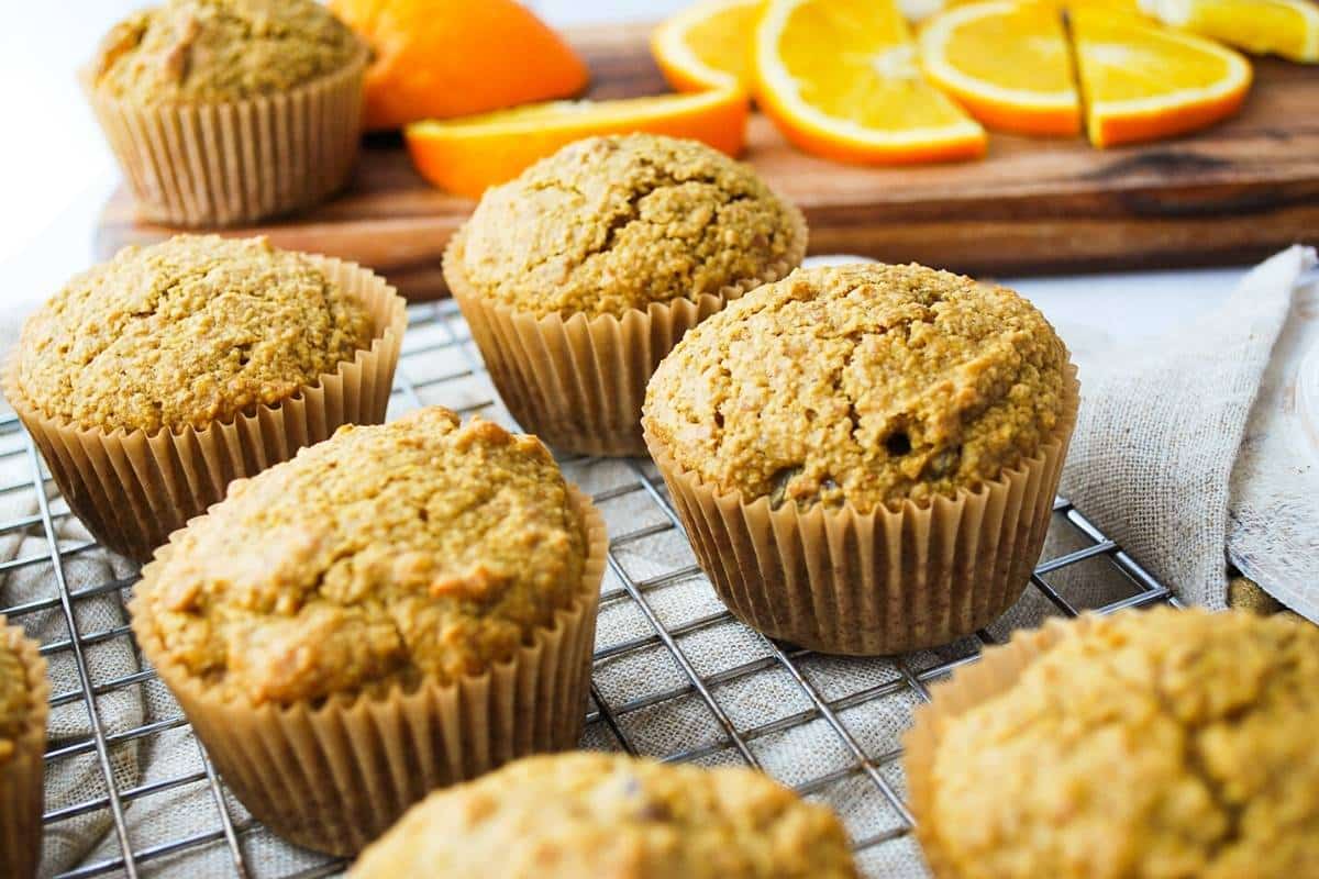 flaxseed muffins on a cooling rack with orange slices on a cutting board in the background