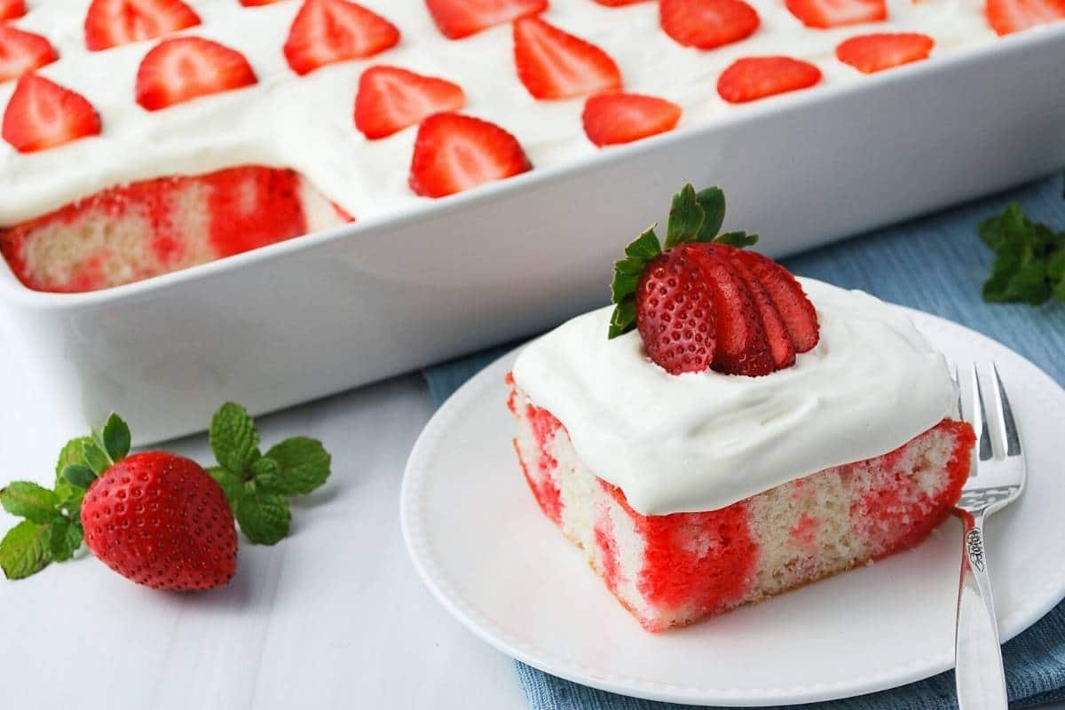 a pan of strawberry jello poke cake with a slice on a plate in front of it