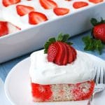 close up of a slice of poke cake with a fork and strawberry garnish on top