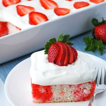 close up of a slice of poke cake with a fork and strawberry garnish on top