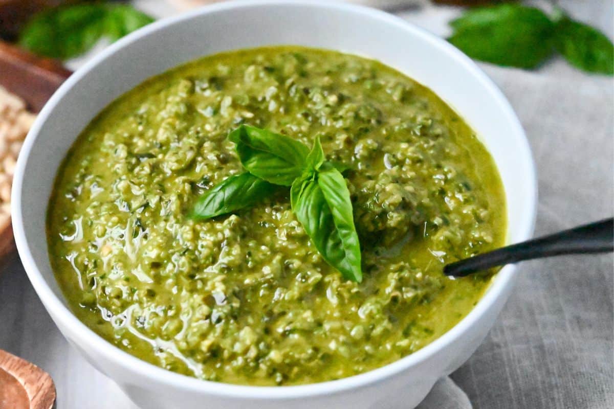 a bowl of basil pesto with fresh basil and a spoon 