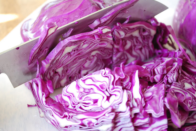 Close up of a knife slicing a head of red cabbage