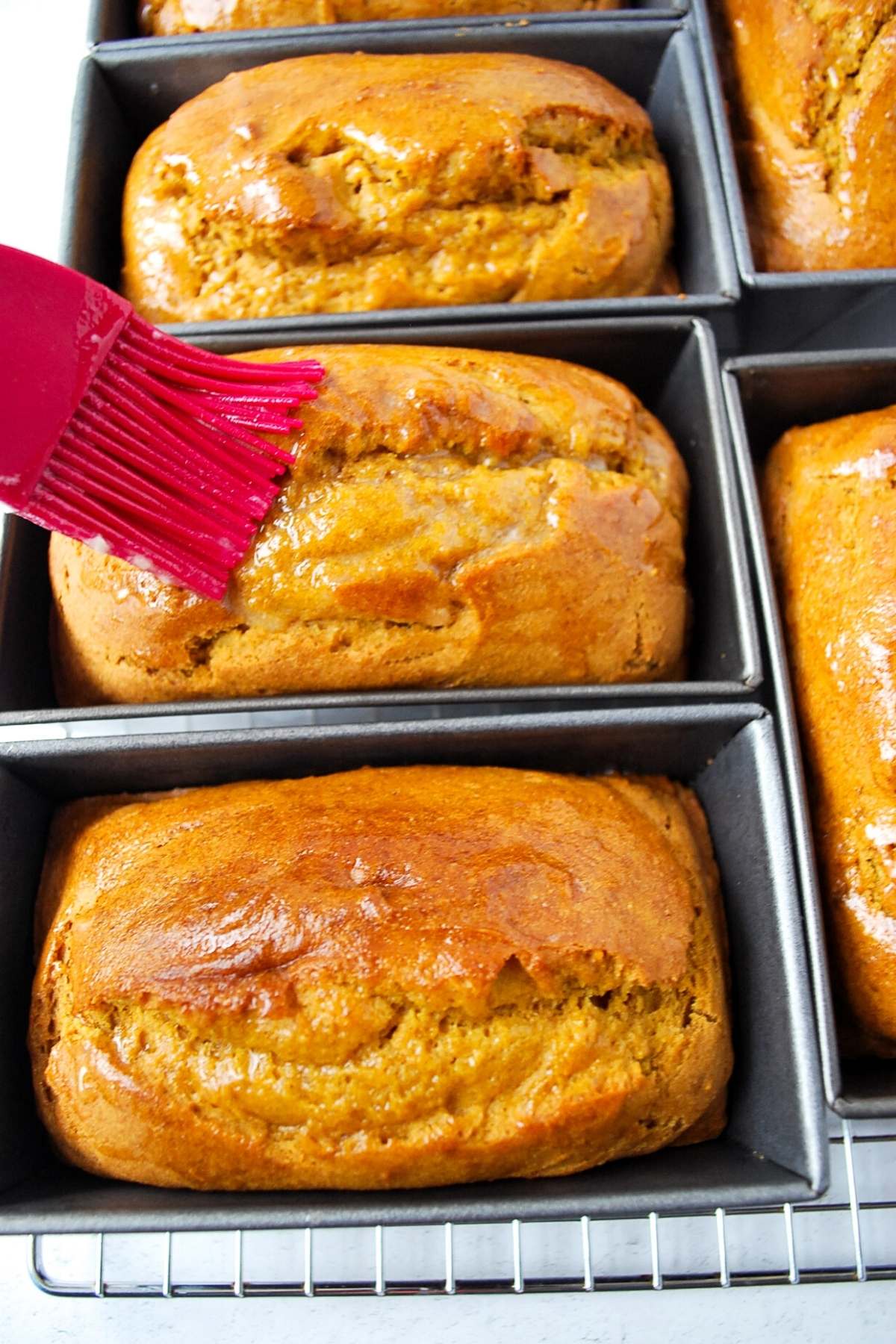 freshly baked pumpkin bread in mini loaf pans getting brushed with butter