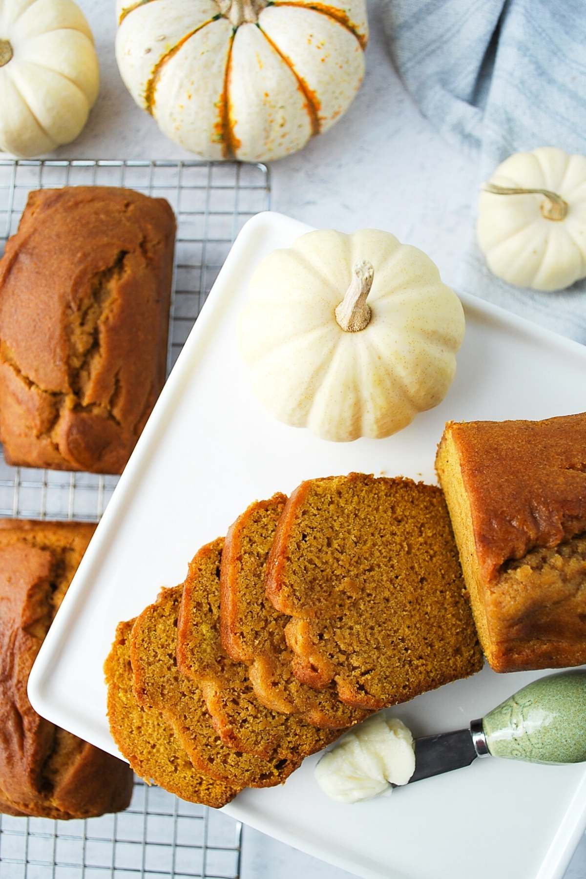 overhead photo of pumpkin bread on a baking rack with a sliced loaf on a platter