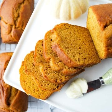 gluten-free pumpkin bread sliced on a platter with a butter knife and mini pumpkin