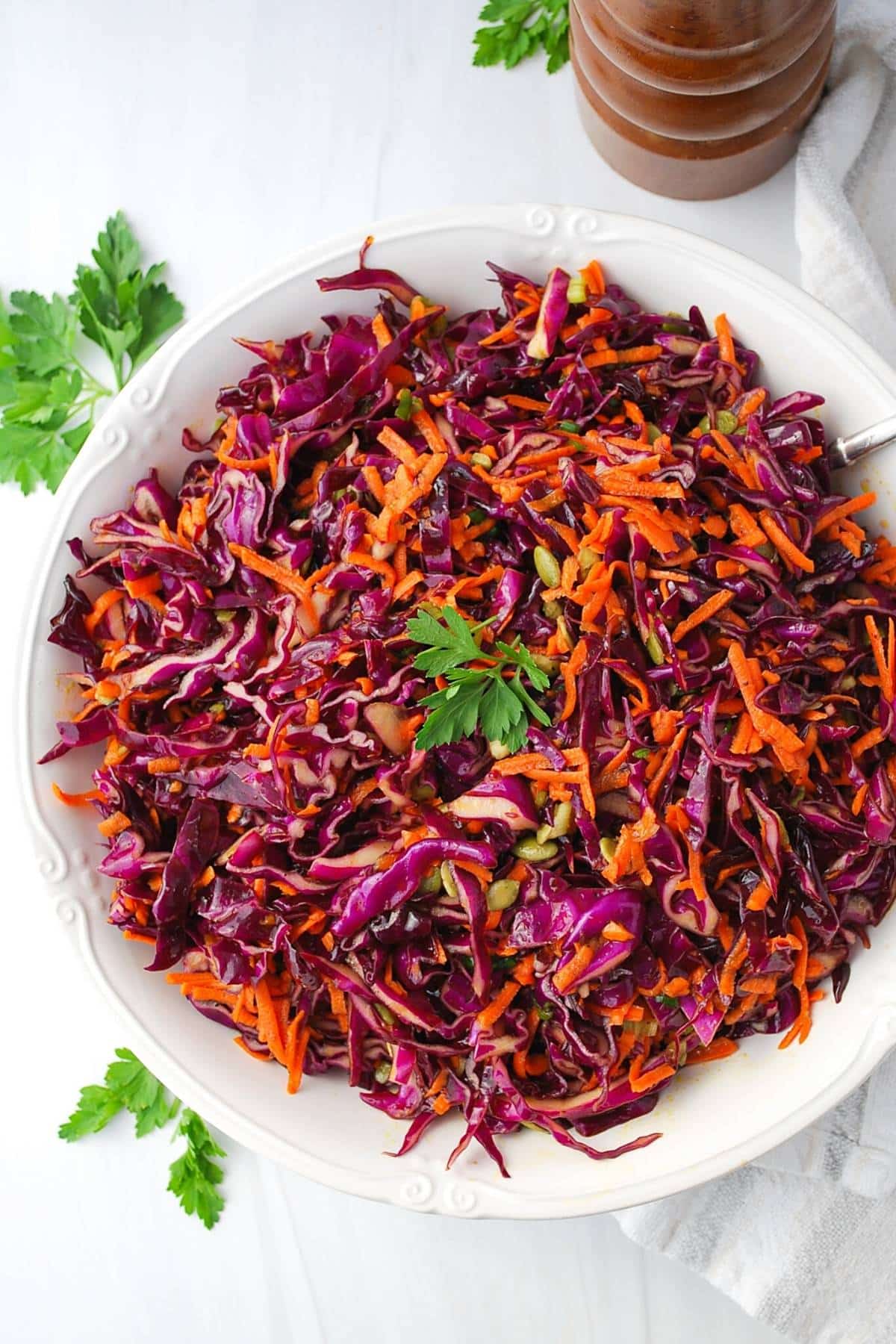 purple coleslaw in a white serving bowl with a peppermill