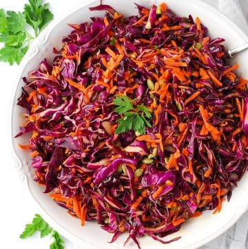 close up photo of a serving bowl of purple coleslaw with a sprig of parsley garnish on top