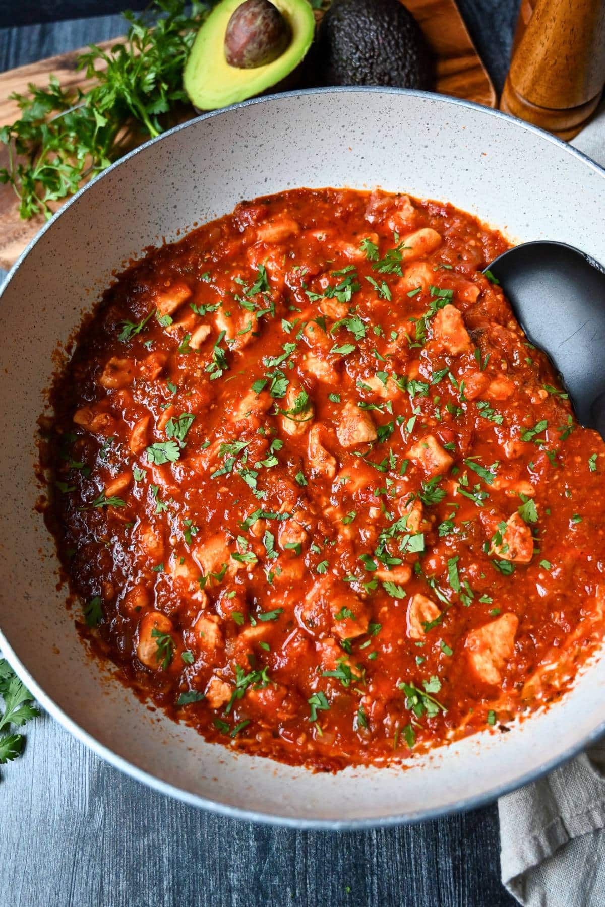 a pan of chicken in a flavorful salsa sauce with a large serving spoon