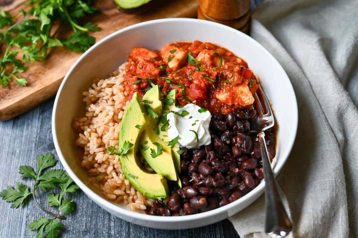 a bowl with chicken in a salsa sauce, rice, beans, avocado and sour cream