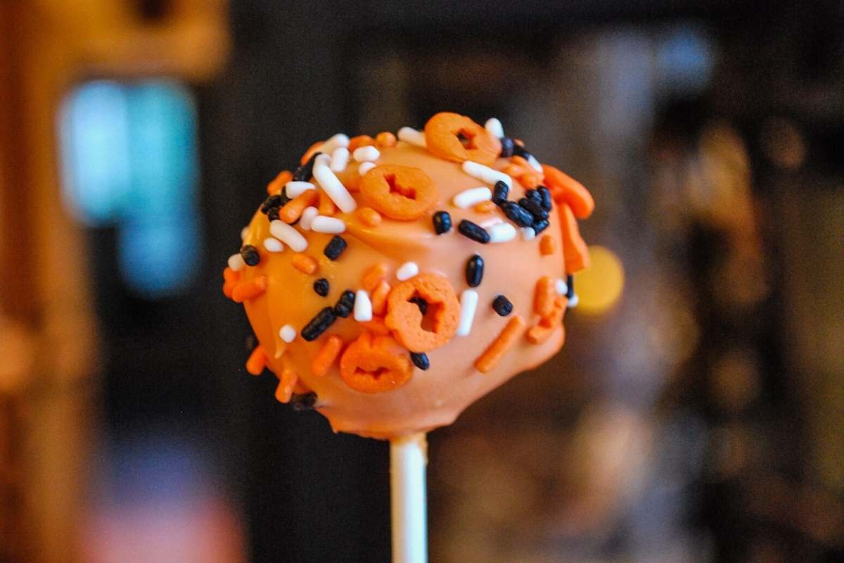 an orange cake pop sprinkled with Halloween confetti sprinkles