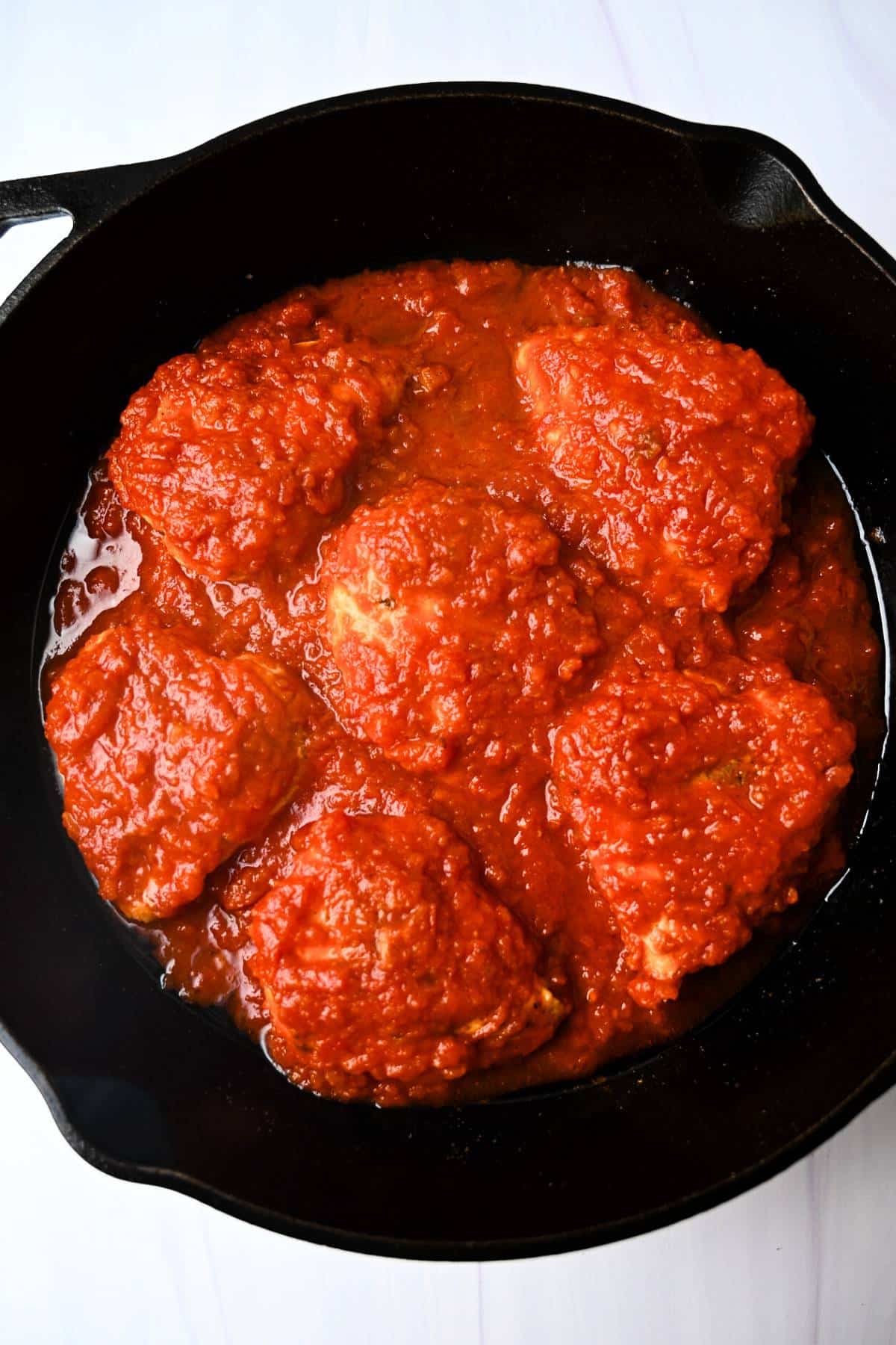 chicken breasts topped with marinara in a cast iron skillet