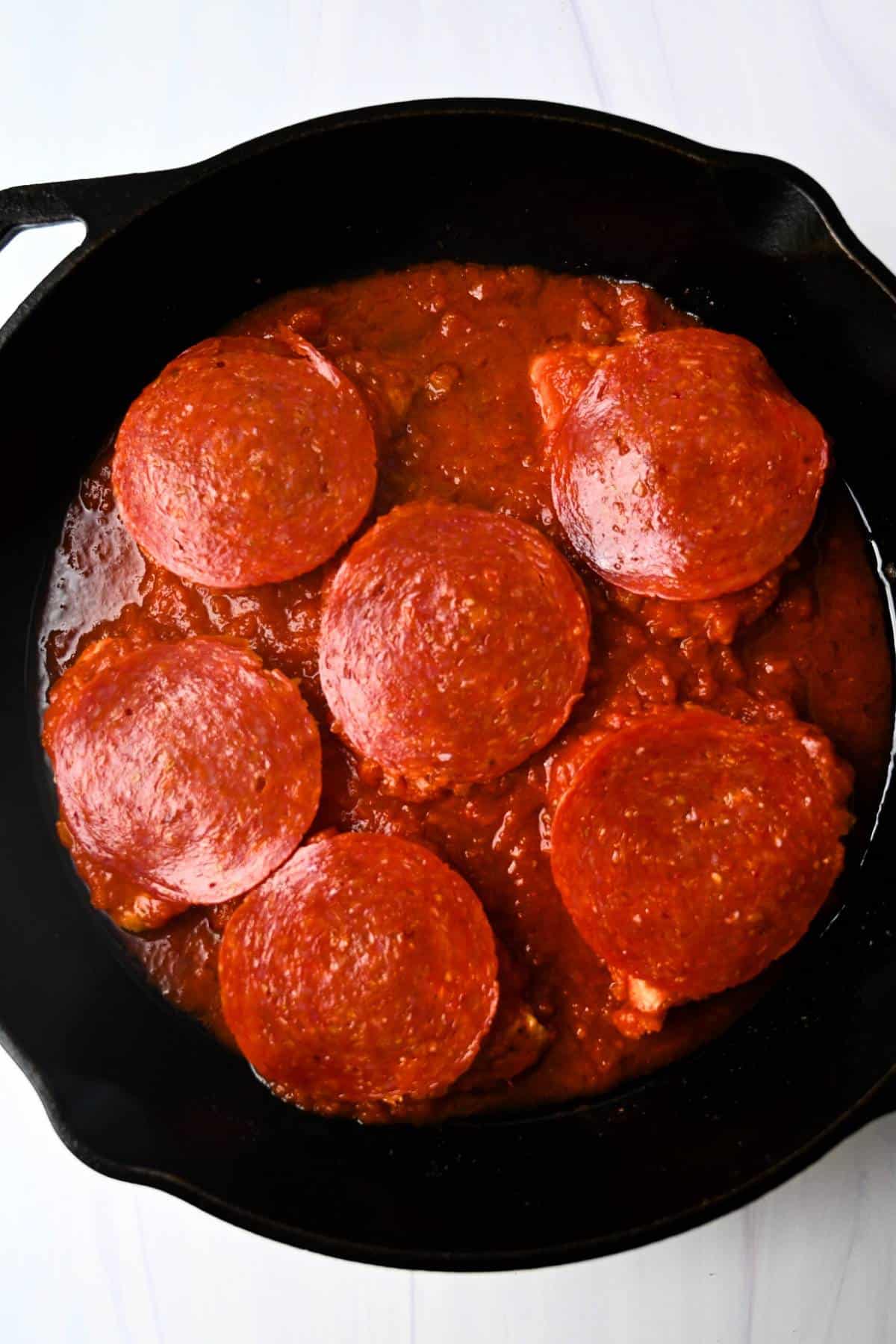 chicken breasts topped with pepperoni in a cast iron skillet