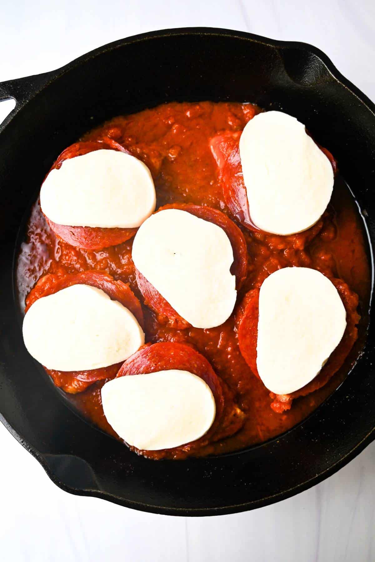 chicken breasts topped with marinara, pepperoni slices, and buffalo mozzarella in a skillet
