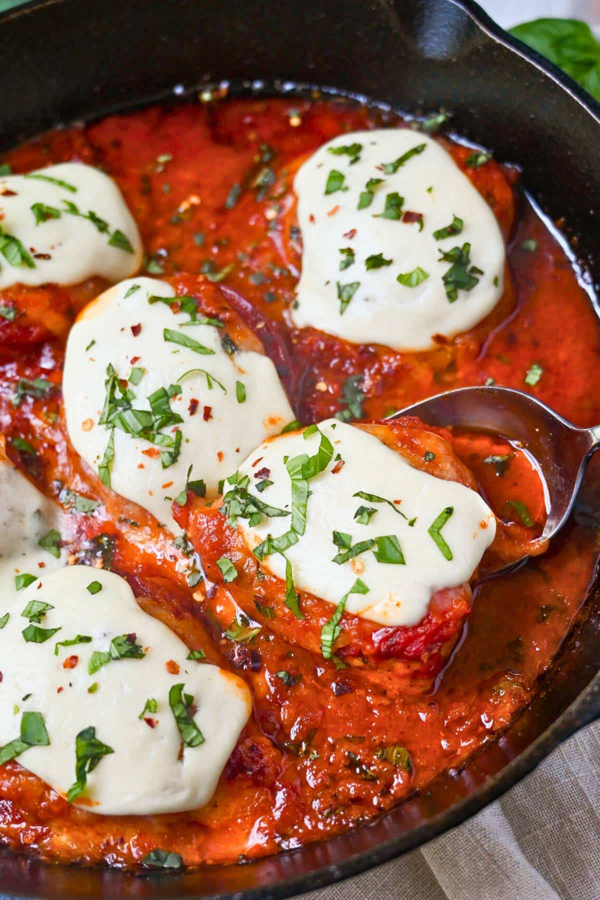 pizza chicken in a cast iron skillet with melted mozzarella on top and fresh basil