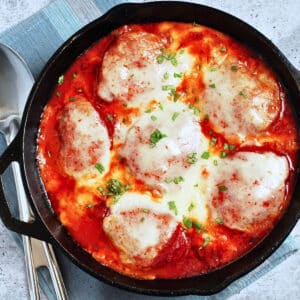 a cast iron skillet with baked pizza chicken and parsley on top