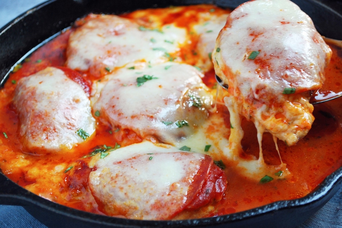 holding up a piece of pizza chicken with melty mozzarella on top