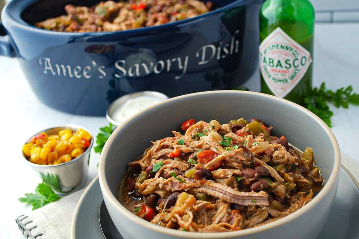 close up of a bowl of pork chili with a jar of Tabasco and corn salsa behind it