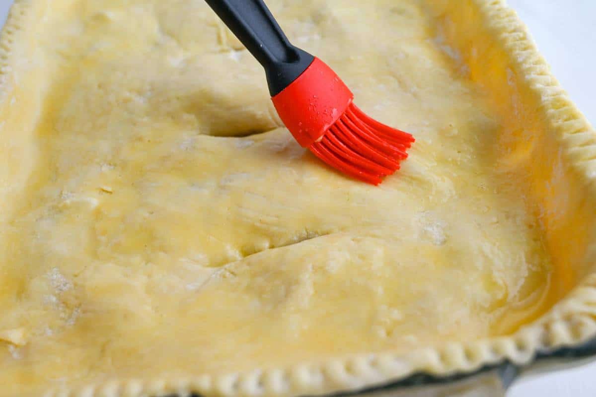 brushing the top of a puff pastry casserole crust with a pastry brush and butter