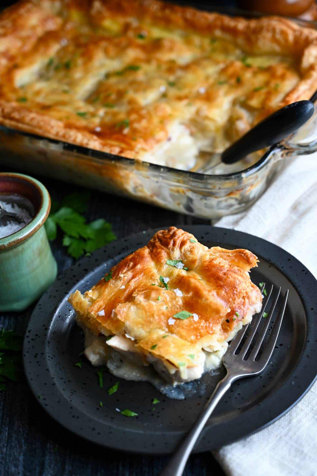 a serving os swiss chicken puff pastry casserole with a jar of salt and casserole pan behind it